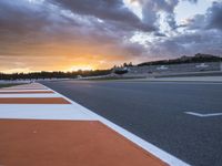 the sun sets in on an airport runway with a cloudy sky above it and some orange stripes