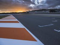 the sun sets in on an airport runway with a cloudy sky above it and some orange stripes