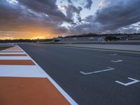 the sun sets in on an airport runway with a cloudy sky above it and some orange stripes