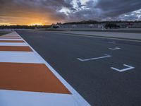 the sun sets in on an airport runway with a cloudy sky above it and some orange stripes