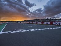 the view from behind the pit looking towards the sky and sunset at a track with a red fence