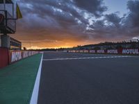 the view from behind the pit looking towards the sky and sunset at a track with a red fence