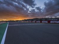 the view from behind the pit looking towards the sky and sunset at a track with a red fence