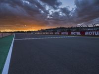 the view from behind the pit looking towards the sky and sunset at a track with a red fence