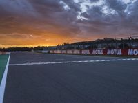 the view from behind the pit looking towards the sky and sunset at a track with a red fence