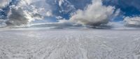 the sky above a large, flat landscape with snow on it, clouds and a sky background