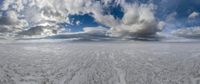 the sky above a large, flat landscape with snow on it, clouds and a sky background