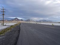 a deserted road and a dry lake surrounded by mountains on the side of it under a stormy sky