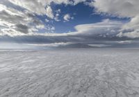 a large cloud is rising over a snow covered beach and distant mountains in the background