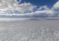 a large cloud is rising over a snow covered beach and distant mountains in the background