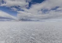 a large cloud is rising over a snow covered beach and distant mountains in the background