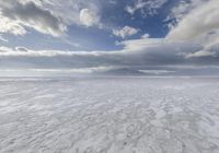 a large cloud is rising over a snow covered beach and distant mountains in the background