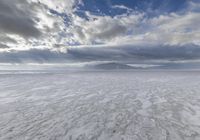 a large cloud is rising over a snow covered beach and distant mountains in the background