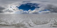 a snow field has a sky and clouds on it below a white sky and a light blue horizon