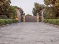 the driveway entrance leads to a gate and outdoor privacy paneled doors, which are lined with greenery