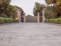the driveway entrance leads to a gate and outdoor privacy paneled doors, which are lined with greenery
