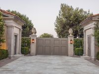 the driveway entrance leads to a gate and outdoor privacy paneled doors, which are lined with greenery