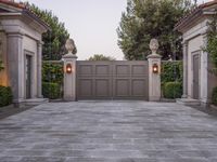 the driveway entrance leads to a gate and outdoor privacy paneled doors, which are lined with greenery