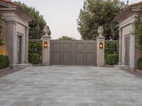 the driveway entrance leads to a gate and outdoor privacy paneled doors, which are lined with greenery