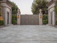 the driveway entrance leads to a gate and outdoor privacy paneled doors, which are lined with greenery