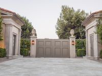 the driveway entrance leads to a gate and outdoor privacy paneled doors, which are lined with greenery