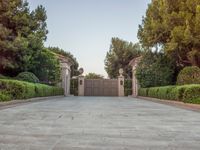 the driveway entrance leads to a gate and outdoor privacy paneled doors, which are lined with greenery