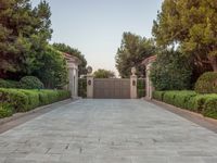 the driveway entrance leads to a gate and outdoor privacy paneled doors, which are lined with greenery