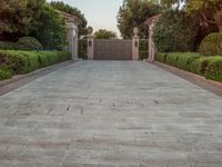 the driveway entrance leads to a gate and outdoor privacy paneled doors, which are lined with greenery