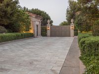 a driveway with bushes and trees in the background and a gate to one side of it