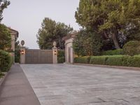 a driveway with bushes and trees in the background and a gate to one side of it