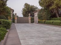 a driveway with bushes and trees in the background and a gate to one side of it