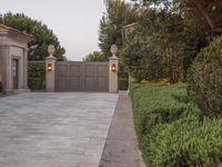 a driveway with bushes and trees in the background and a gate to one side of it