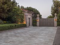 a driveway with bushes and trees in the background and a gate to one side of it