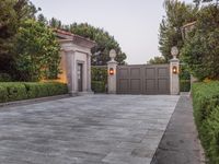 a driveway with bushes and trees in the background and a gate to one side of it