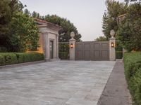 a driveway with bushes and trees in the background and a gate to one side of it
