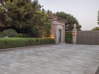a driveway with bushes and trees in the background and a gate to one side of it