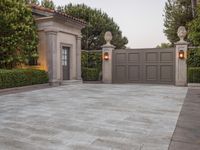a driveway with bushes and trees in the background and a gate to one side of it