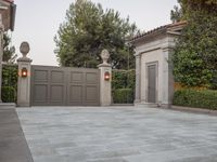 a driveway with bushes and trees in the background and a gate to one side of it
