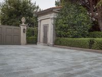 a driveway with bushes and trees in the background and a gate to one side of it