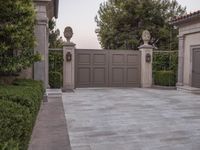 a driveway with bushes and trees in the background and a gate to one side of it