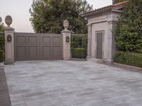 a driveway with bushes and trees in the background and a gate to one side of it