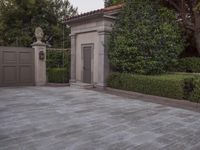 a driveway with bushes and trees in the background and a gate to one side of it