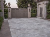 a driveway with bushes and trees in the background and a gate to one side of it