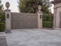 a driveway with bushes and trees in the background and a gate to one side of it