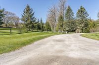 a paved driveway leading into a tree lined field with lots of green grass and trees