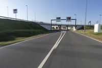 the car is driving down the road beside a tunnel with street signs above it on a sunny day