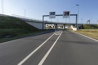 the car is driving down the road beside a tunnel with street signs above it on a sunny day