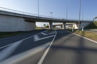 the car is driving down the road beside a tunnel with street signs above it on a sunny day