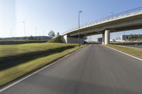 the car is driving down the road beside a tunnel with street signs above it on a sunny day