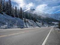 an empty highway stretches from the mountain to the street with snow on it and evergreens covering a mountain